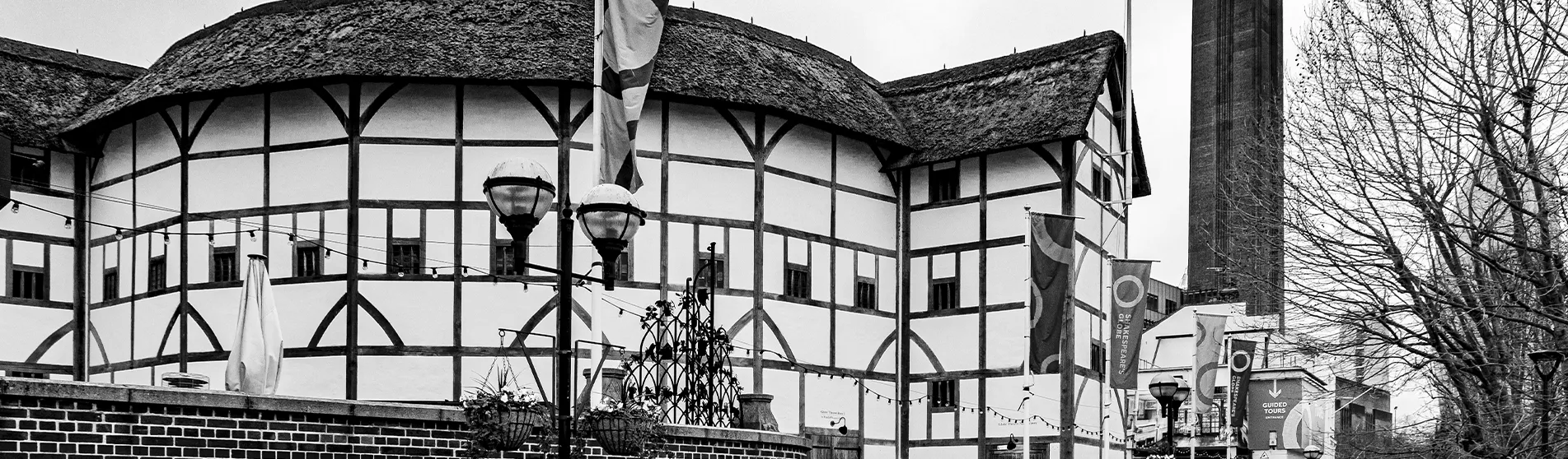 A black and white image of The Globe Theatre in London, an Elizabethan building with an iconic circular structure, taken from the outside.