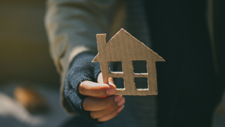 Person experiencing homelessness holding a cardboard cutout of a house