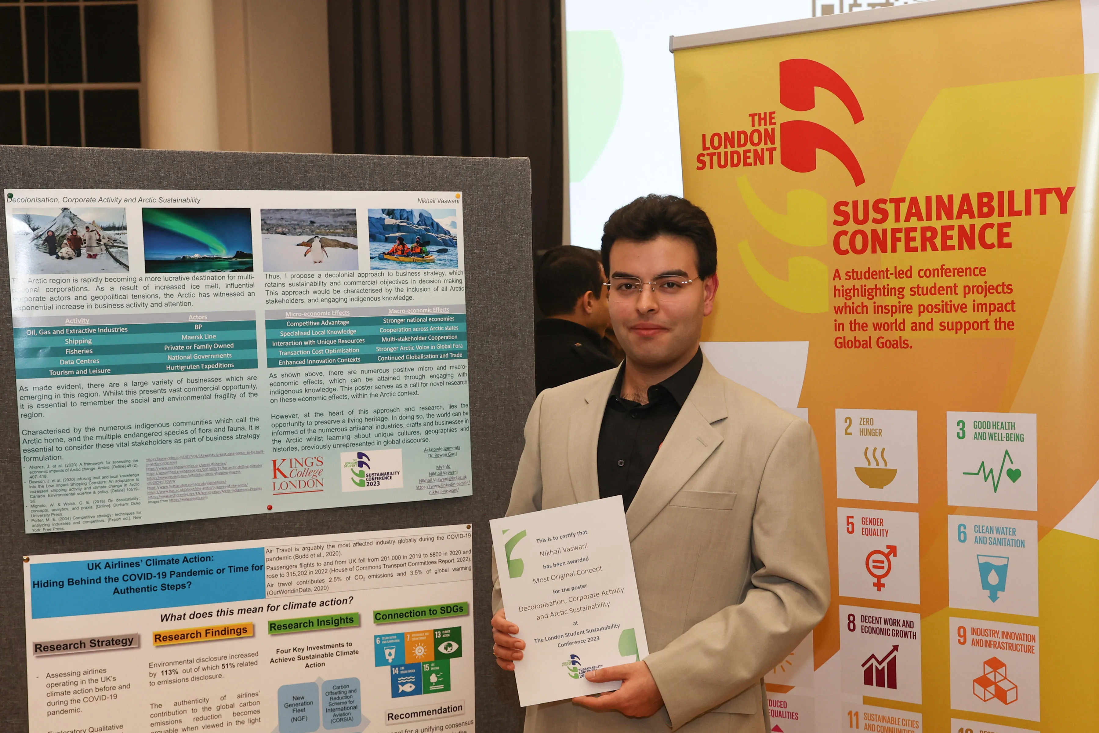 Nikhail Vaswani holding up his award in front of his poster.