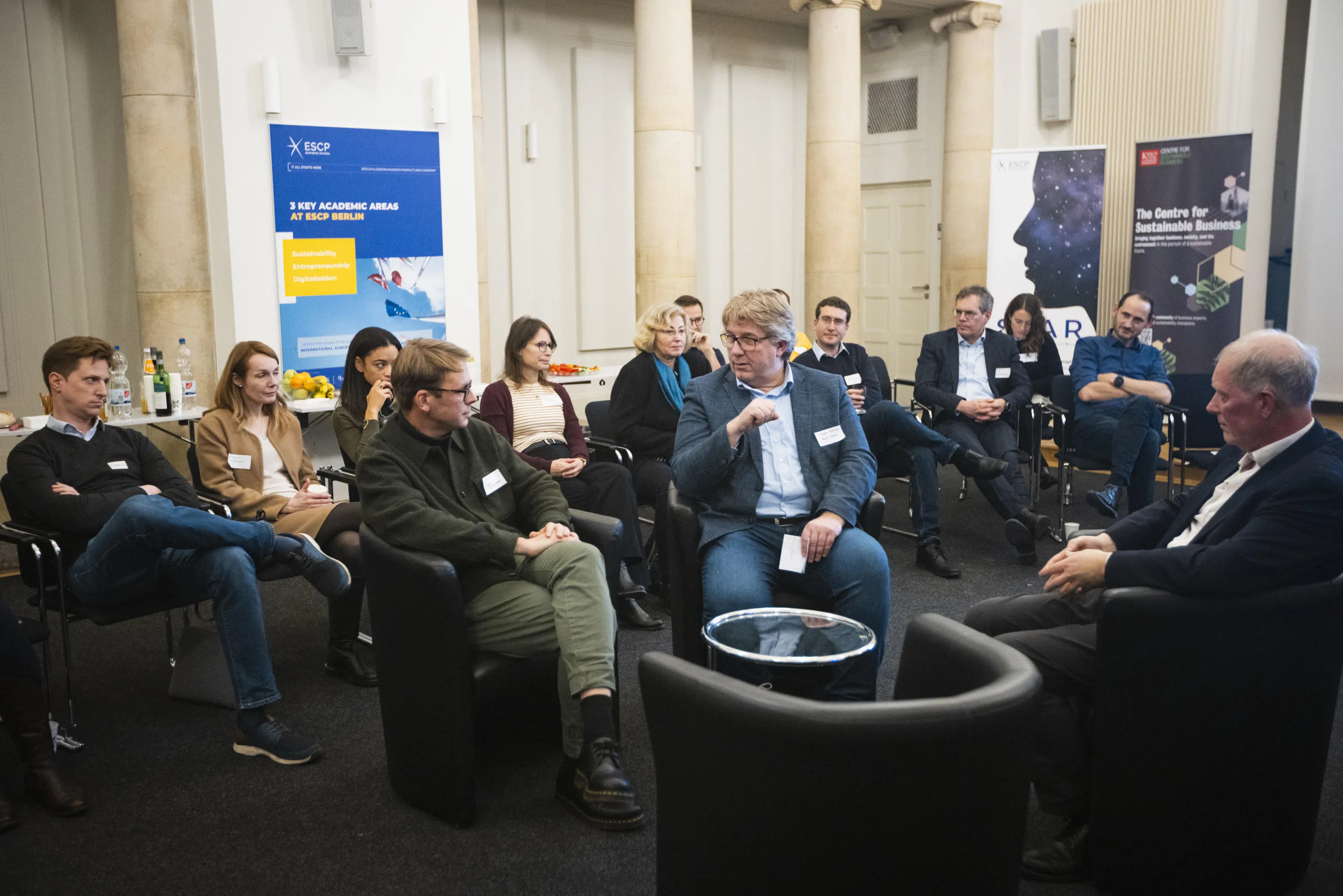 Three men sit in chairs in the middle of the event to discuss key issues in AI.