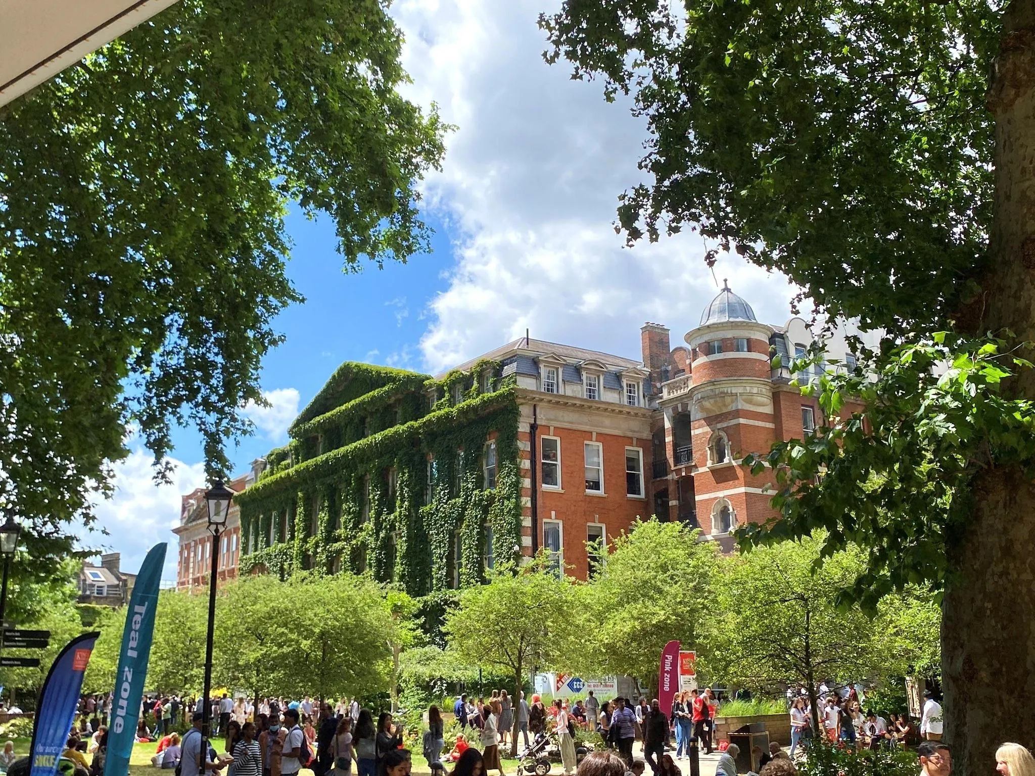 King's College London's Guy's Campus on a sunny day, trees frame the image and the building is covered in wall climbing plants.