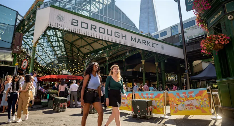 Two women smiling and walking through Borough Market with the Shard in the background.