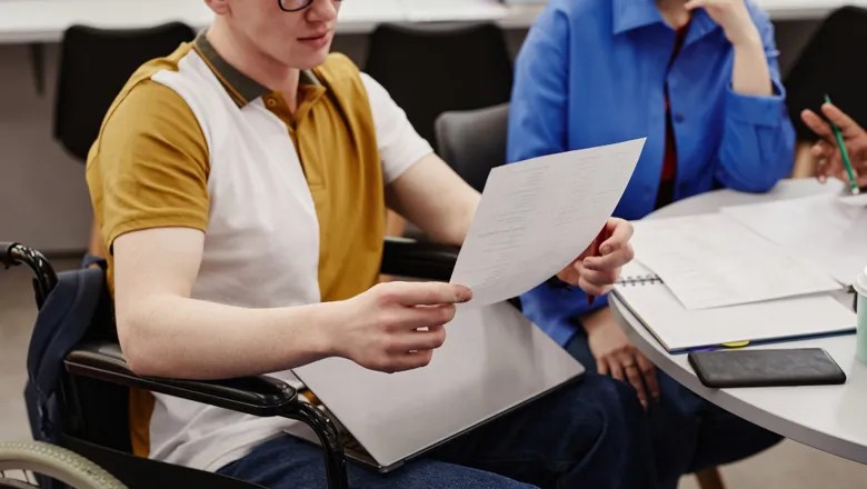 Cropped shot of a student in a wheelchair reading notes while studying with a group of friends.