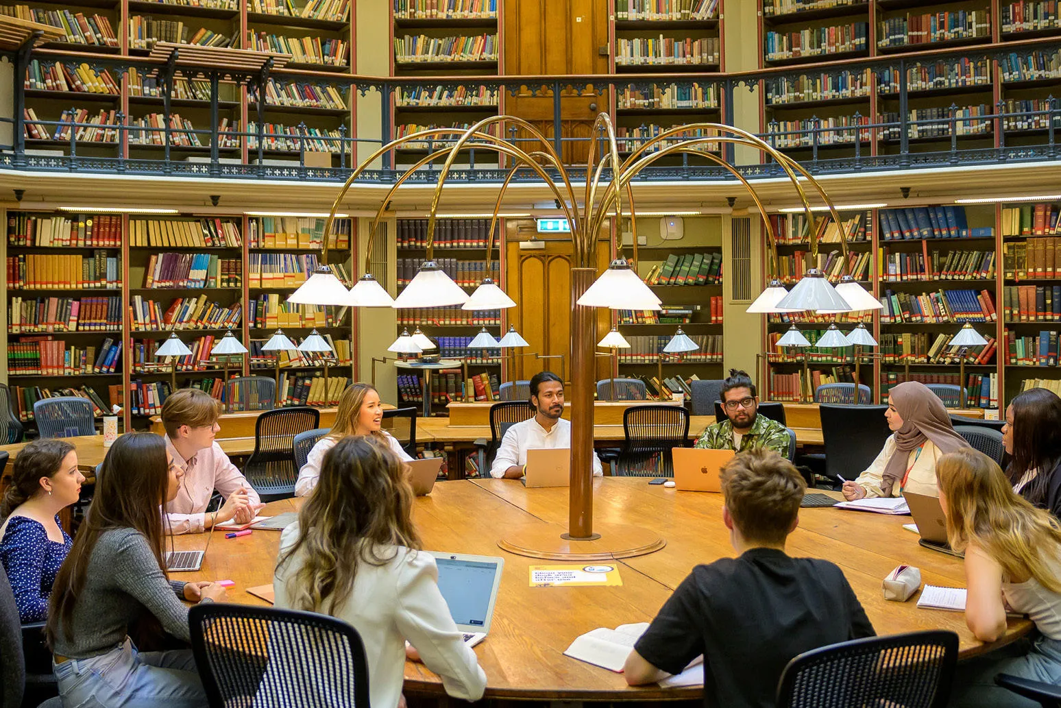 A group of students sitting around a circular table with laptops and books in the Maughan library