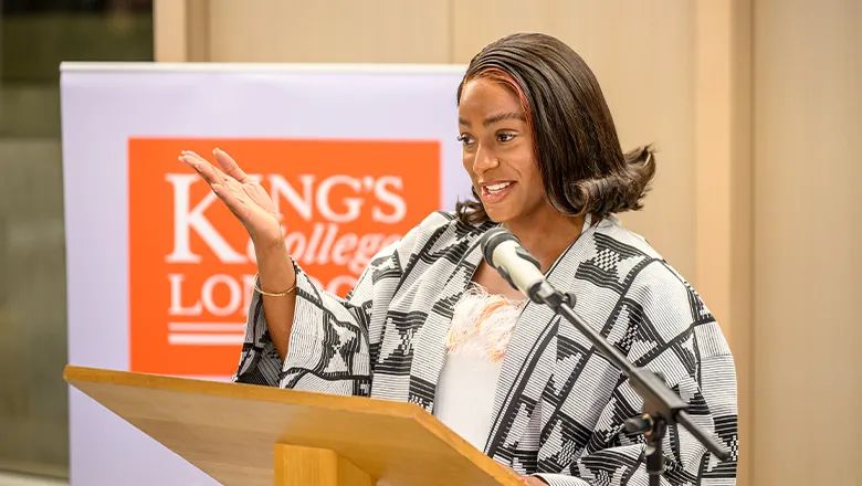 Cuppy holds her hand outstretched welcomingly as she speaks at an event.