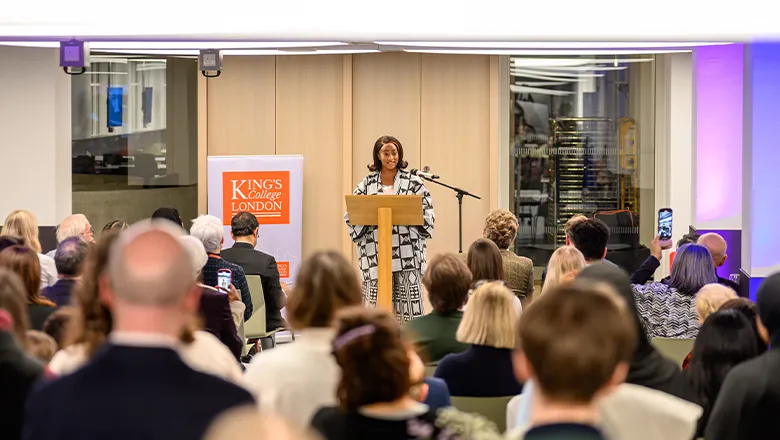 Cuppy stands at a lectern, speaking to a room full of people.