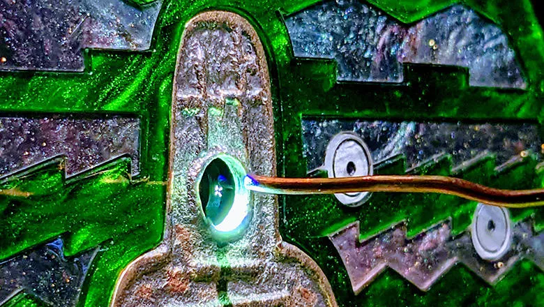 An image of a microchip, with copper wire and jagged green designs