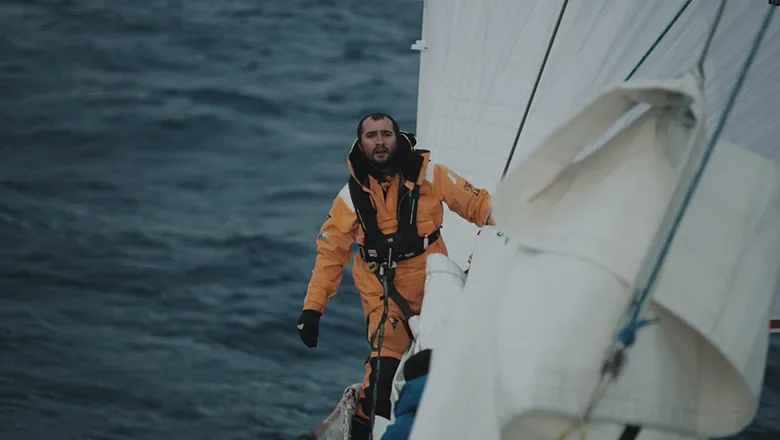 Afshin Ahmadian hangs off a white canvas sail on his boat in the middle of the ocean.