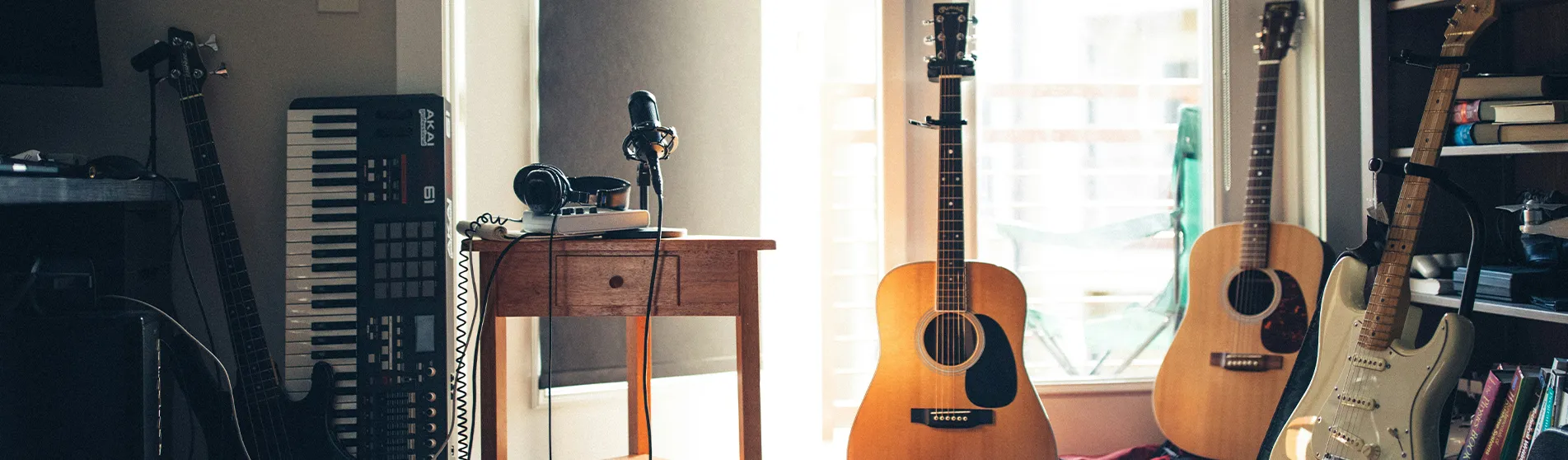 A room filled with various musical instruments, including two acoustic guitars, a keyboard propped up against a wall, a white electric guitar and a black bass