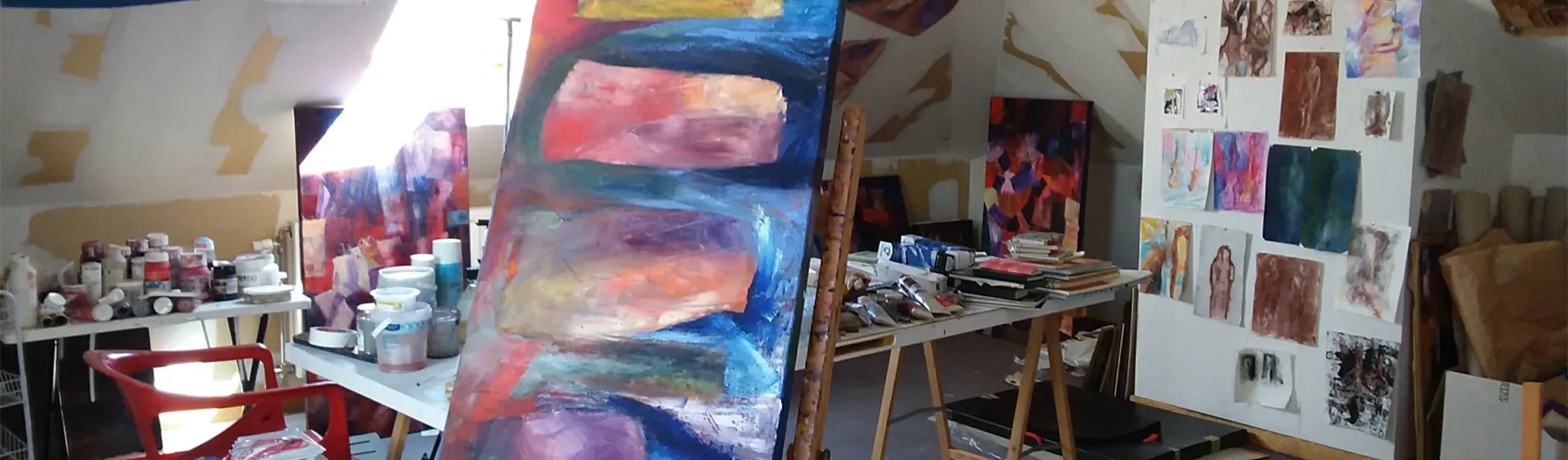 An art studio, full of paintings on easels and paint jars