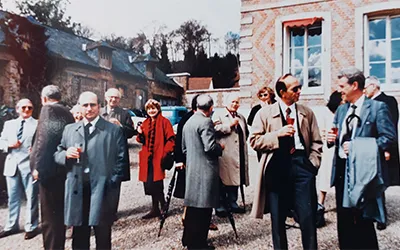 An 80s photo of a reunion, with people standing in a courtyard sipping drinks and talking