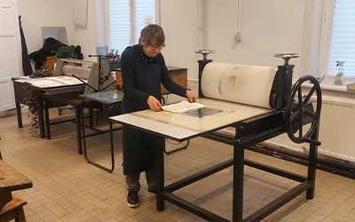 A woman stands at an old printing press