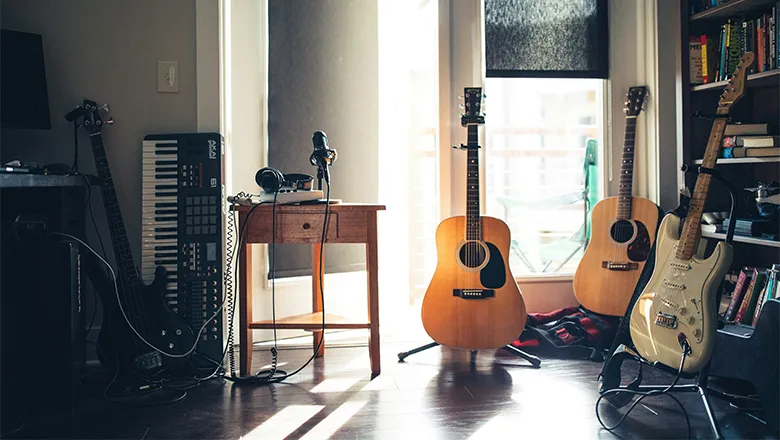 A room filled with various musical instruments, including two acoustic guitars, a keyboard propped up against a wall, a white electric guitar and a black bass