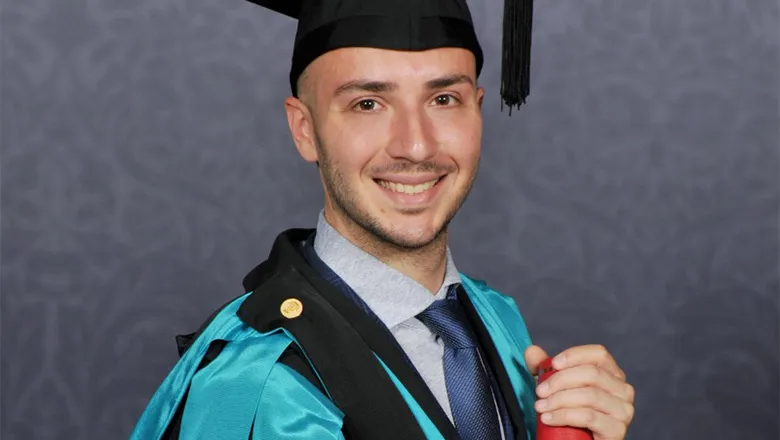 A young man looking very happy in graduation robes holding his degree certificate