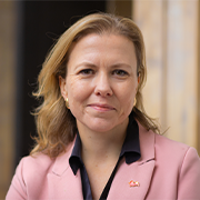 A woman with long hair, wearing a pink blazer, smiles warmly