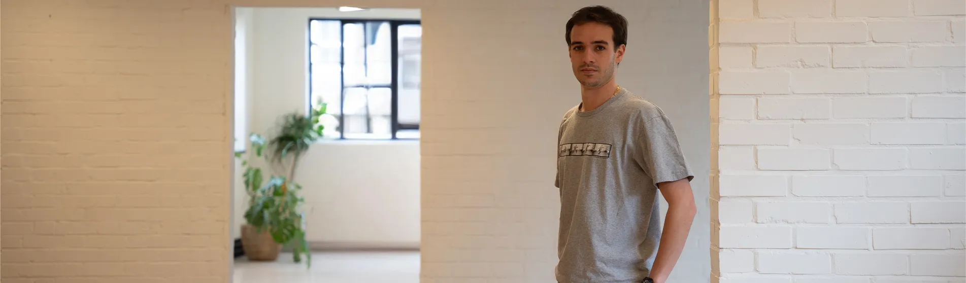 A young man with dark hair wearing smart and casual clothes stands in a clean and uncluttered office space.