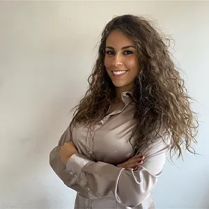 A young woman with long, dark hair and wearing a cream blouse smiles at the camera