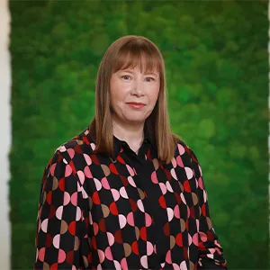 A woman with medium-length brown hair, wearing a vibrant top of red, pink, white and black