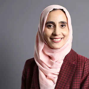 A young woman wearing a red coat and a pink headscarf smiles at the camera