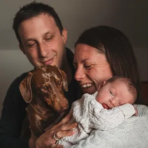 Matteo and Rachel holding their young baby and dog, a brown sausage