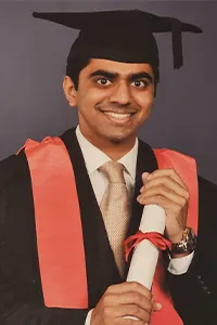 A young man dressed in graduation robes and wearing a mortar board holds a degree certificate