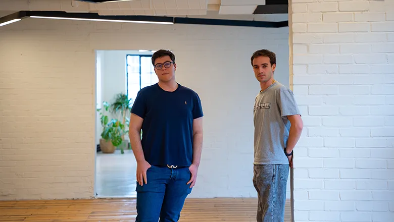 Two young men wearing smart and casual clothes stands in a clean and uncluttered office space.