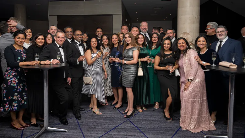 A large group of smiling people in evening wear pose for the camera