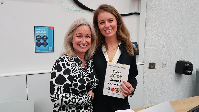 Two women stand together and smile and look relaxed. They hold a book titled Every Body Should Know This by Dr Federica Amati