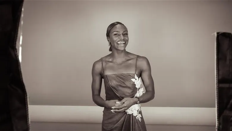 A young woman in a stylish dress with a flower print down one side smiles at the camera