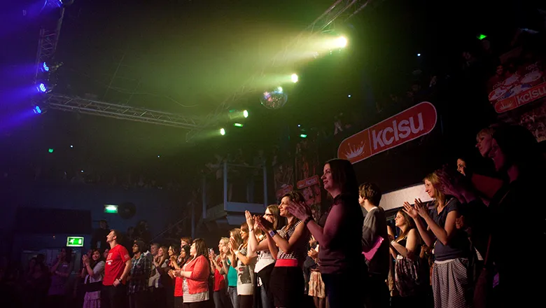 A crowd of people applaud in an indoor music venue