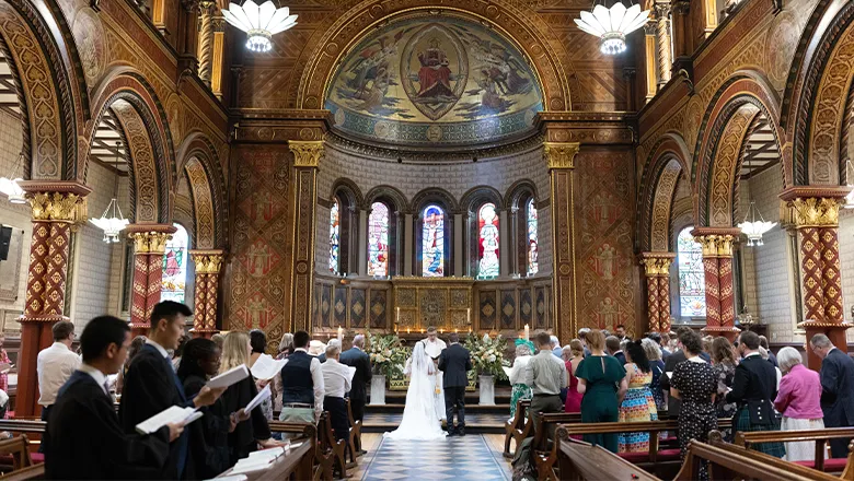 A wedding scene in King's college chapel, in which the groom and bride stand at the altar and the congregation stands