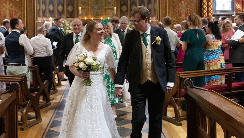 A newly married couple walk down the aisle holding hands as the congregation in attendance applauds