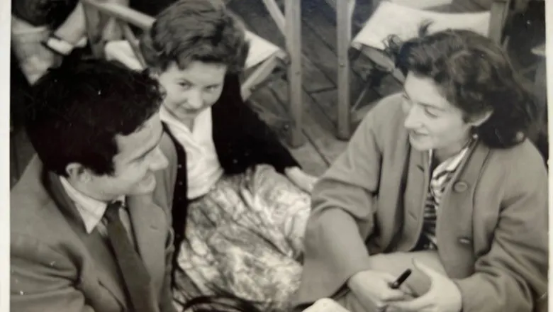 A black and white photograph of a man, with dark hair, and two women in conversation