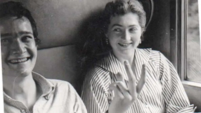 A man and a woman, both smiling widely, sit in an old train carriage