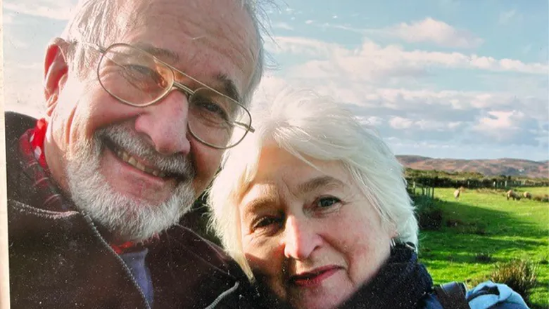 An older couple take a selfie in front of a lush, green countryside background