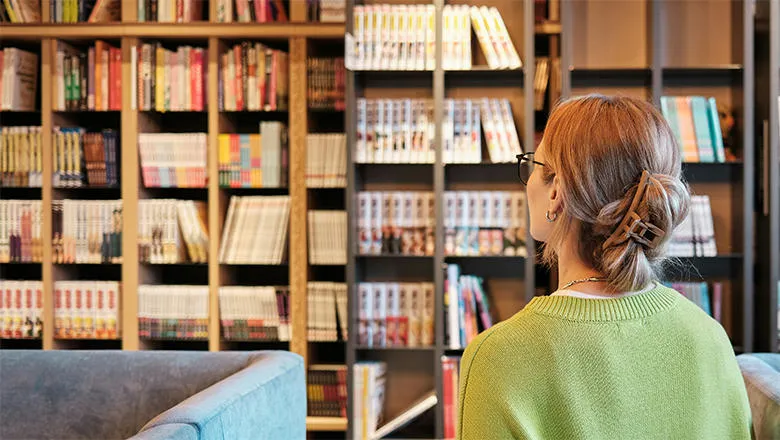 An image of the back of a woman's head as she surveys a shelf of books