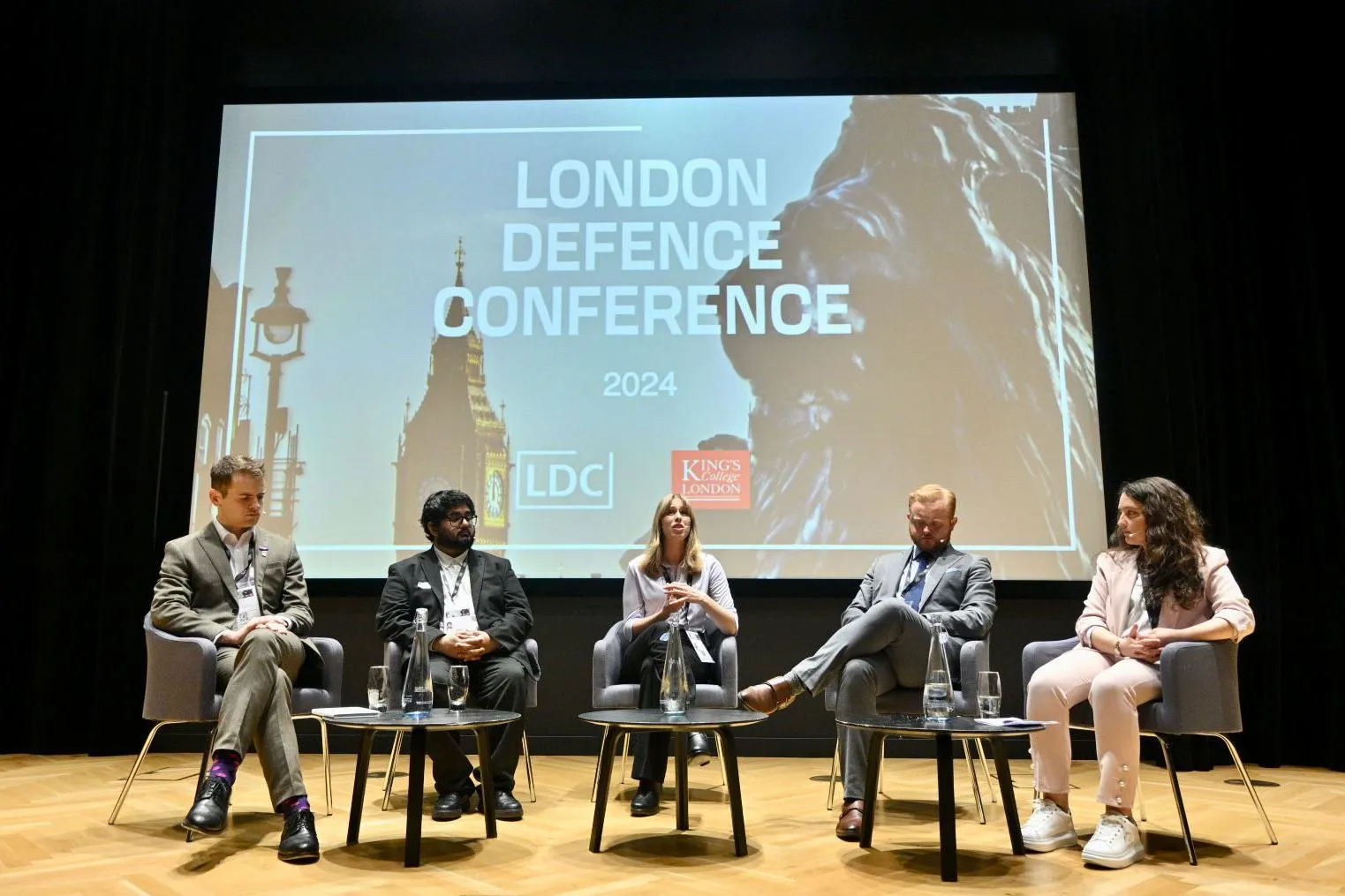 A panel discussion - a row of people seated in front of a large screen reading 'London Defence Conference 2024'