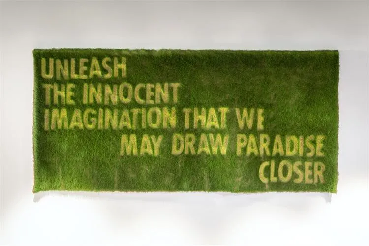 A art installation made from grass with the text unleash the innocent imagination that we may draw paradise closer a quote by Sir Ben Okri