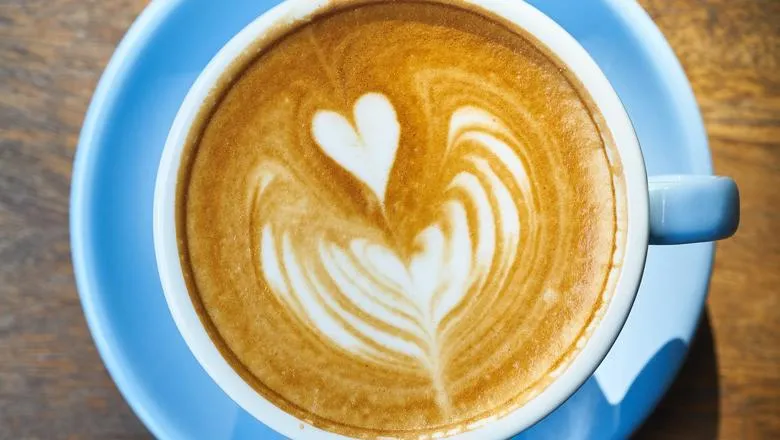 Cappuccino in blue cup with saucer on a wooden table with a heart shape in the froth