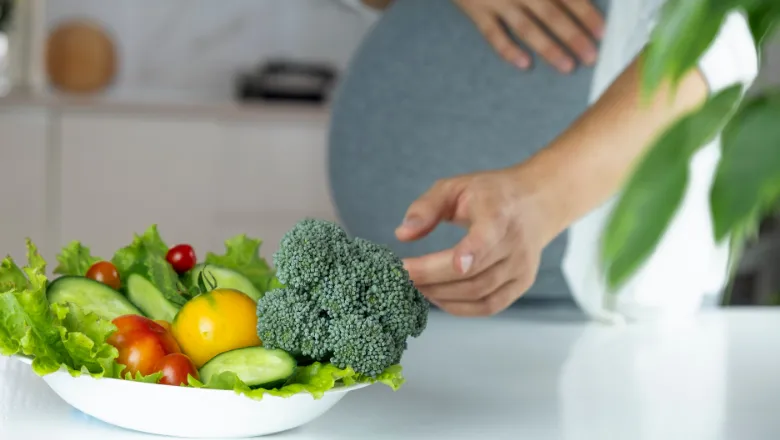 A pregnant person reaching towards a bowl of vegetables.