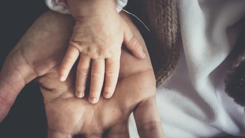 Infant's hand on top of parent's hand.