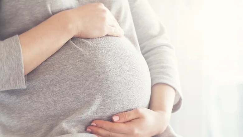 Pregnant woman holding hands on her belly.