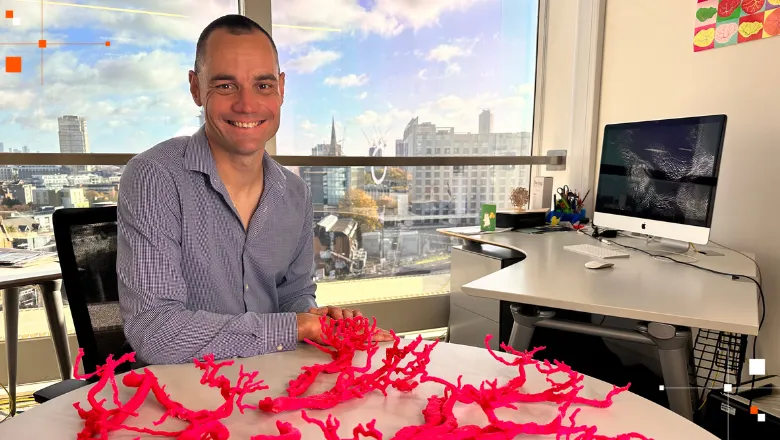 A man sitting in an office with the London skyline in the window behind him