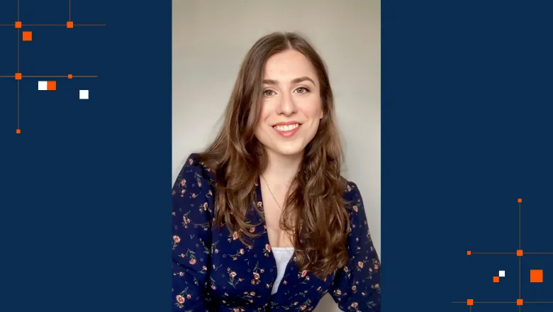 A woman with long, brown hair smiles at the camera.She is wearing a blue floral-patterned blouse and is set against a light-coloured background.