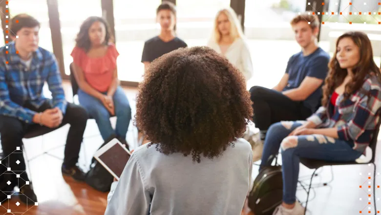 Rear view of female tutor leading discussion group amongst young people.