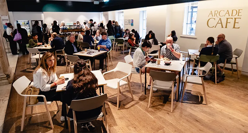 A busy cafe scene, with people sitting and chatting at chairs and tables