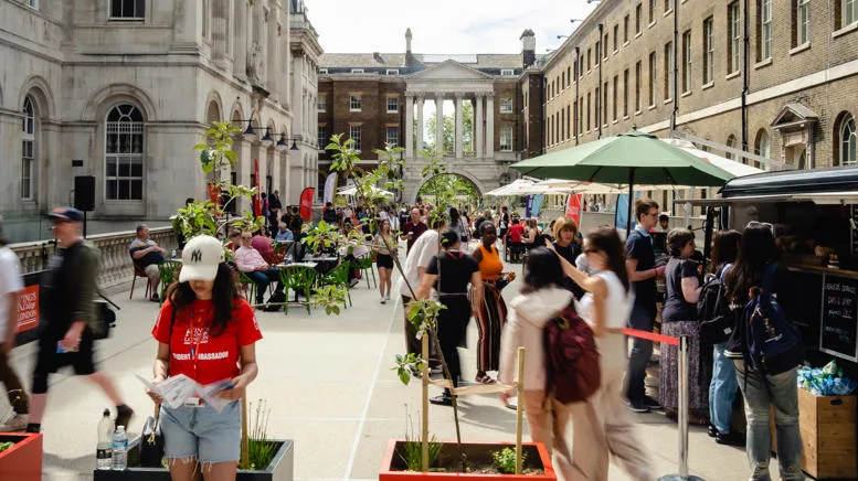 A quad courtyard, with people queuing at a van selling coffee, and chatting in conversation
