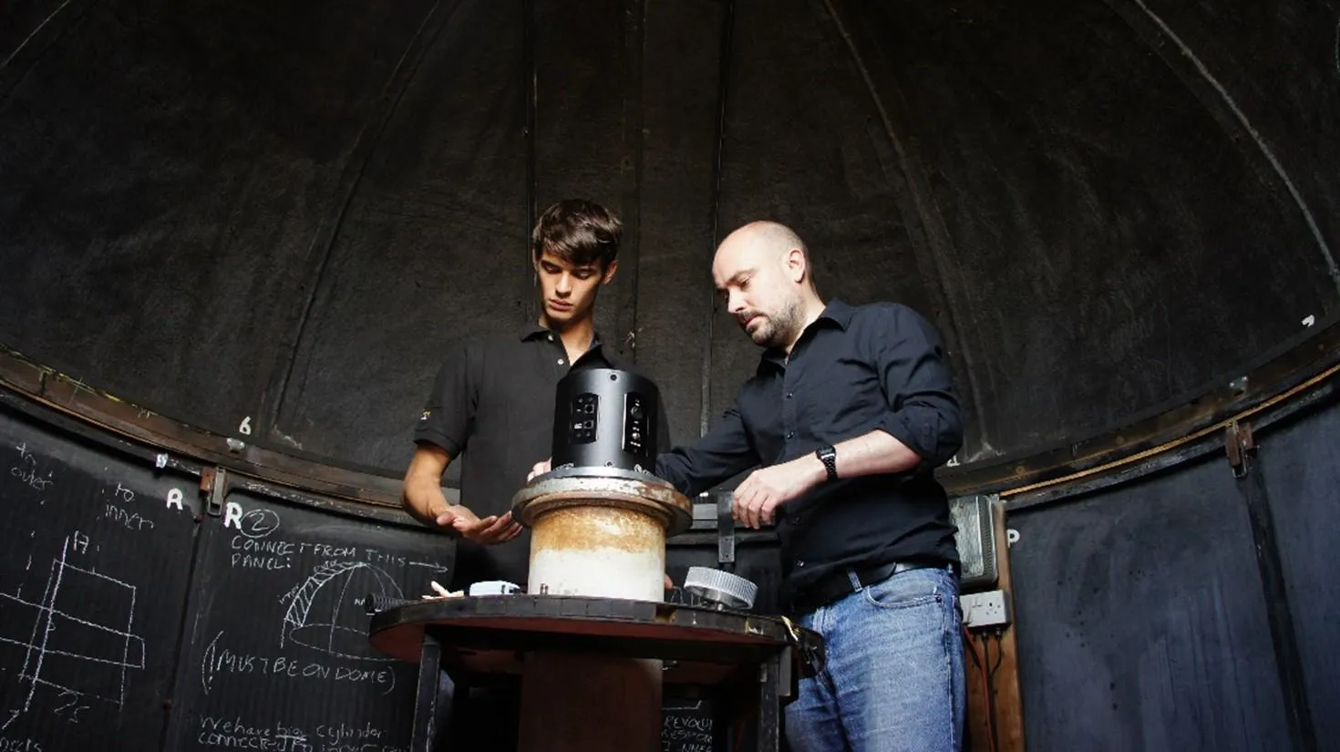 Two people looking at telescope equipment in a domed room