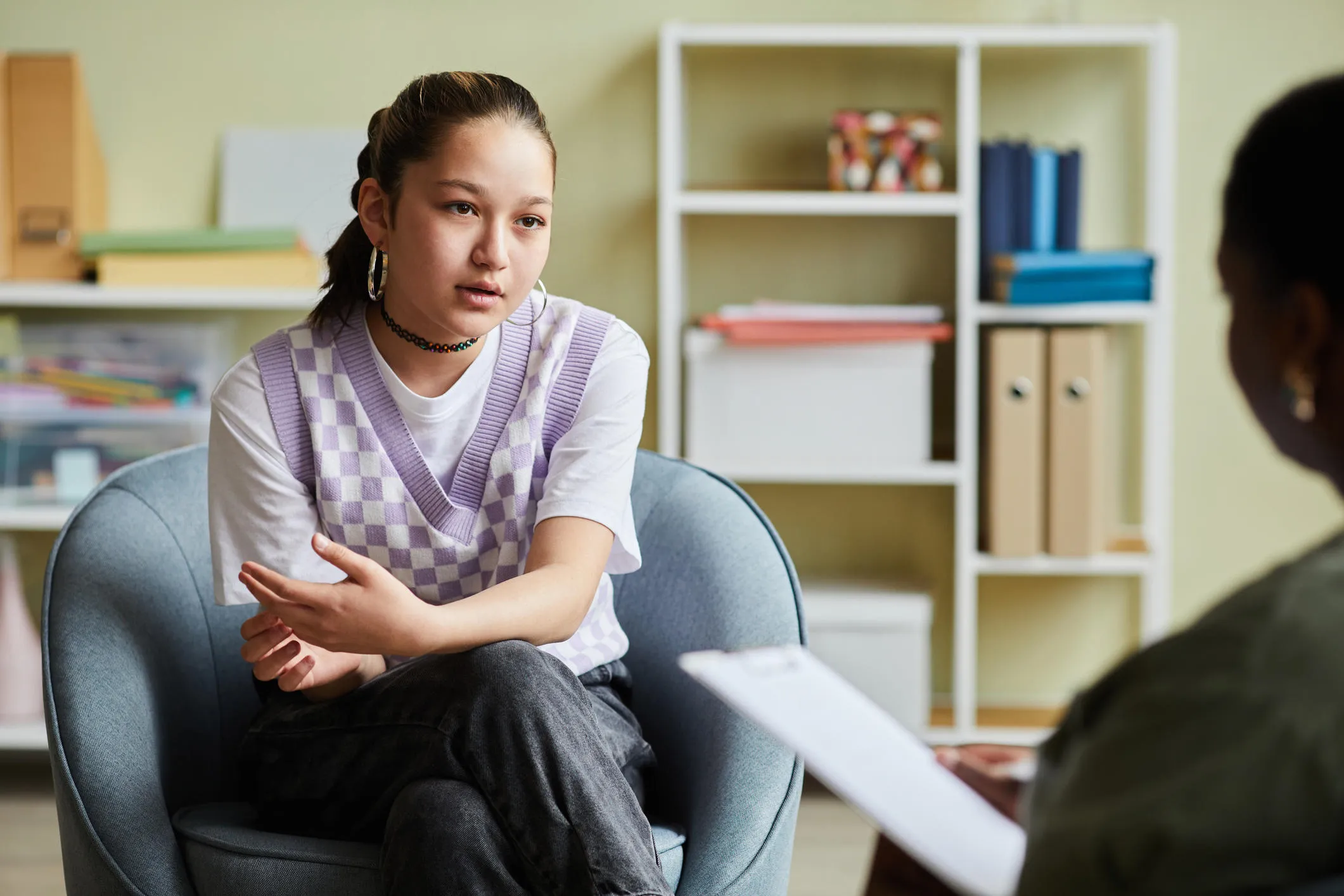 Teenage girl sat in therapy session with clinician holding clipboard