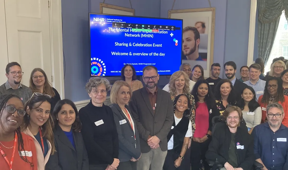 A group of researchers standing together in front of a screen, having participated in a Mental Health Implementation Network event.